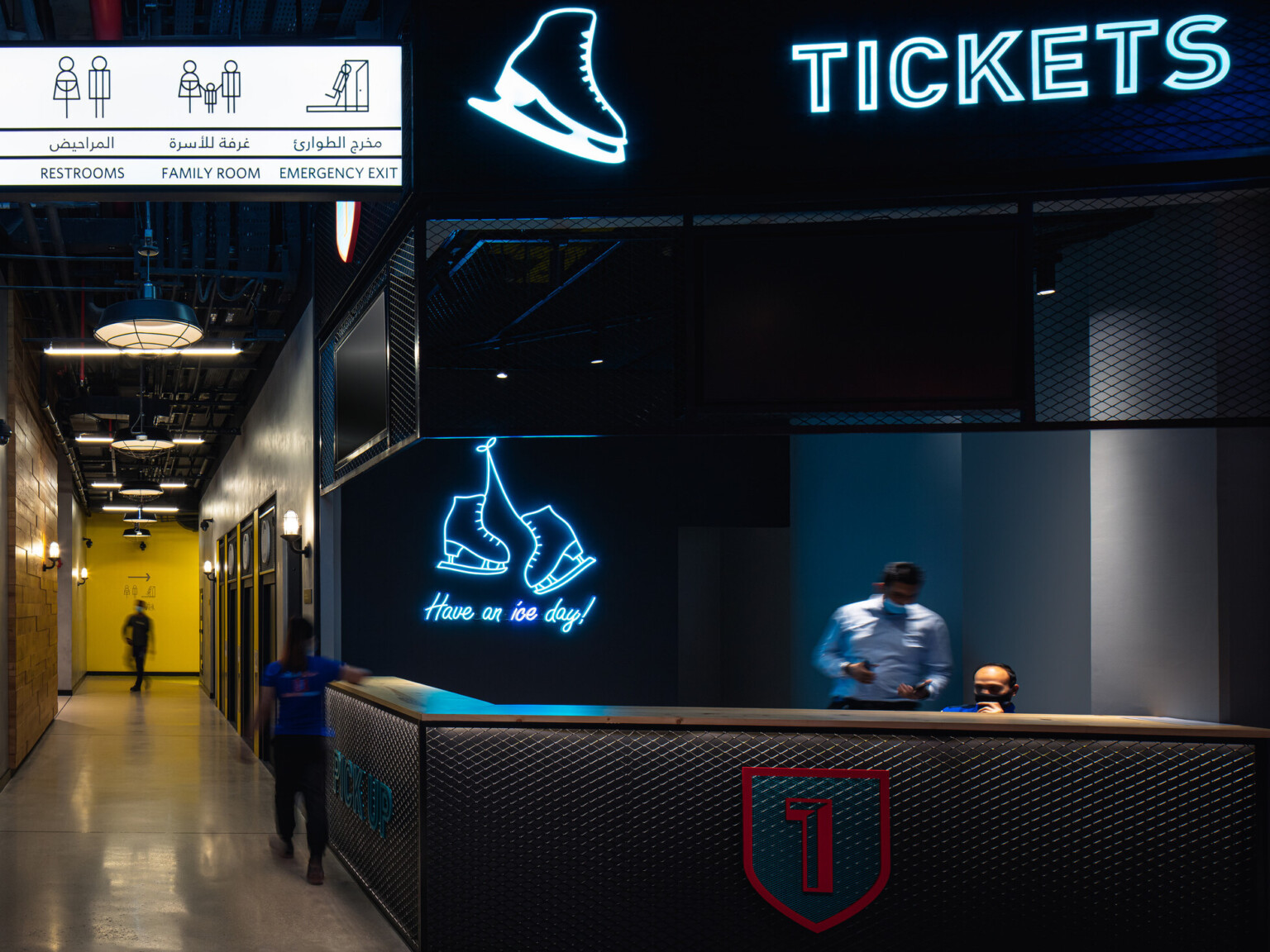 Ticket counter for ice rink with dark walls, directional signage, and blue neon lighting