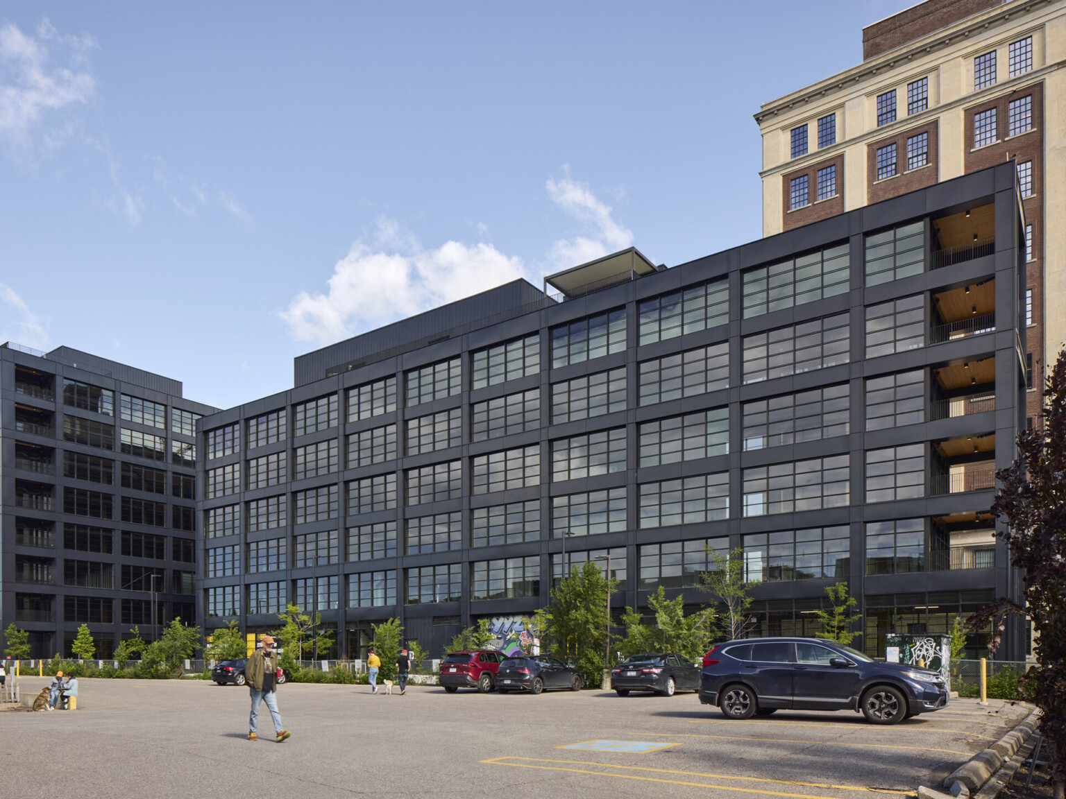 Black multistory office building filled with windows in front of a larger multistory office building