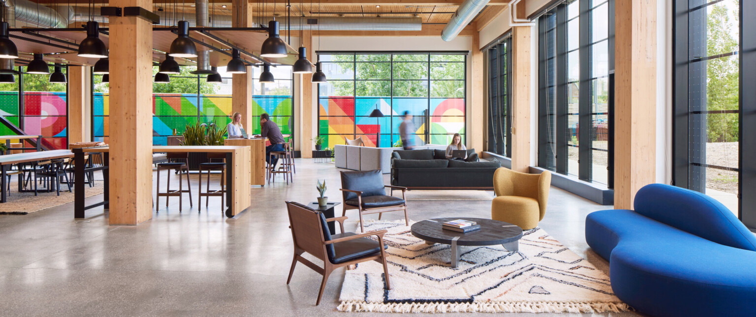 Large office space with exposed wooden beams, floor to ceiling black framed windows, and colorful mural outside