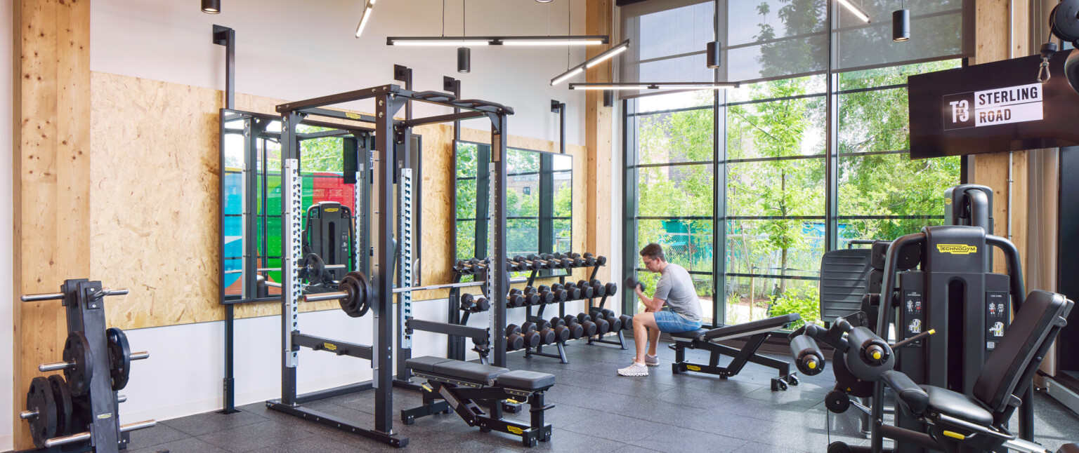 Indoor gym filled with exercise equipment, large black framed floor to ceiling windows and wooden accents throughout