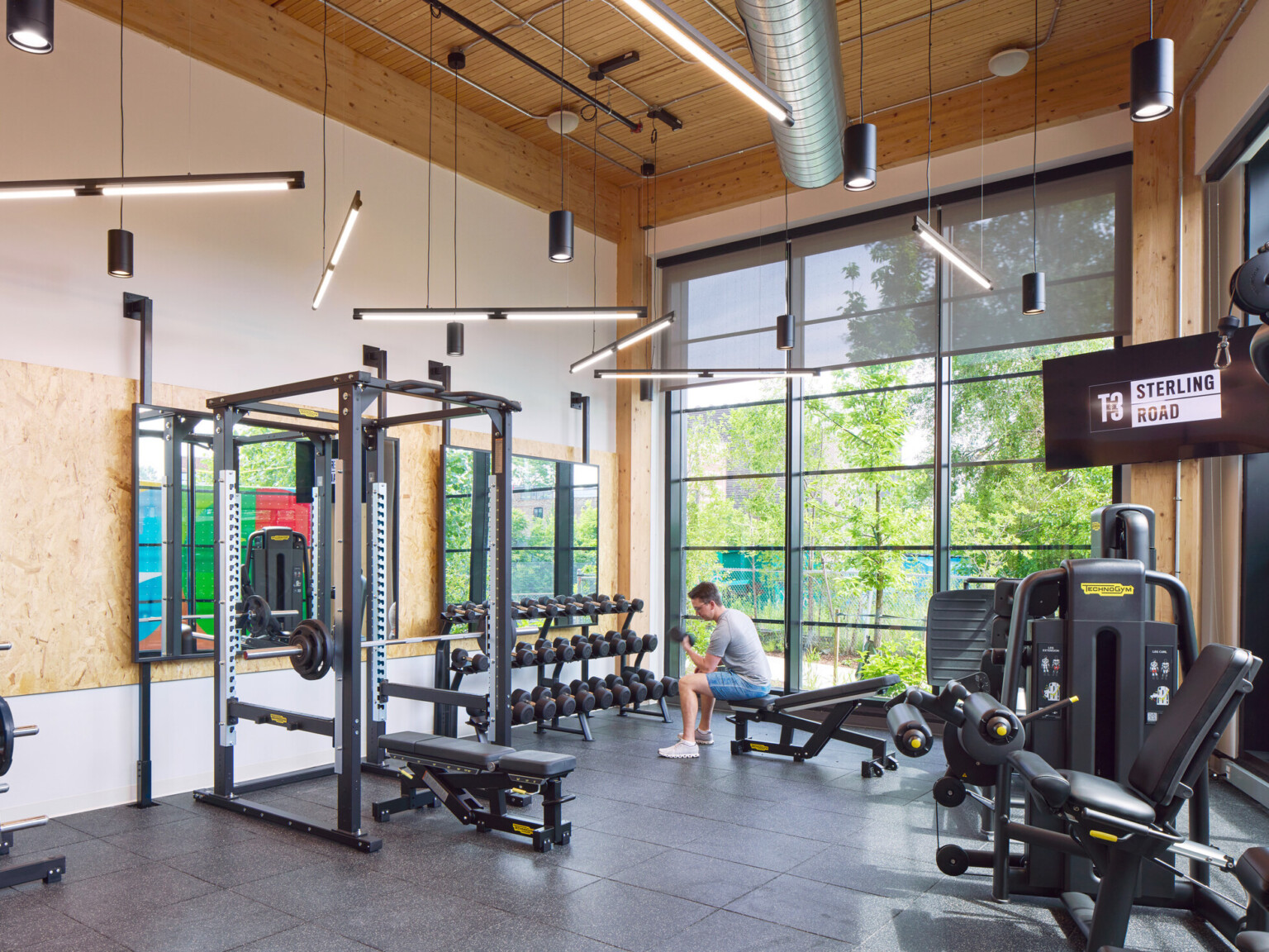 Indoor gym filled with exercise equipment, large black framed floor to ceiling windows and wooden accents throughout