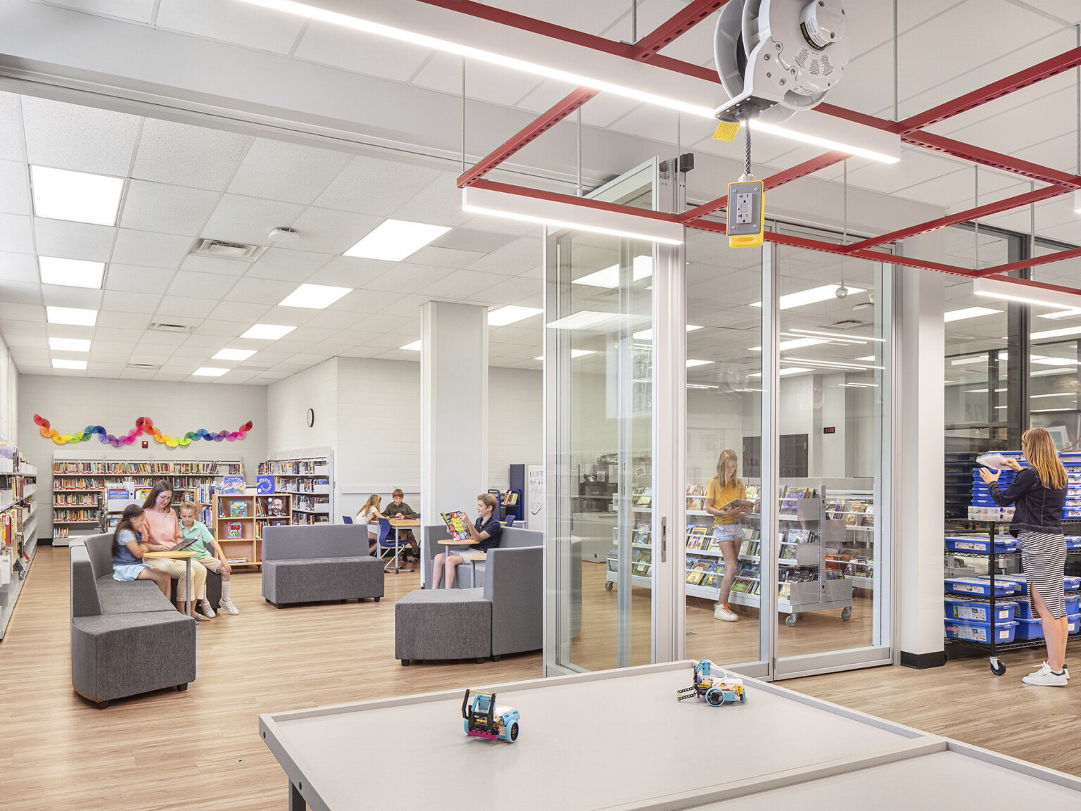 A modern library with glass walls, modular seating, and bookshelves filled with books. People are reading around the room