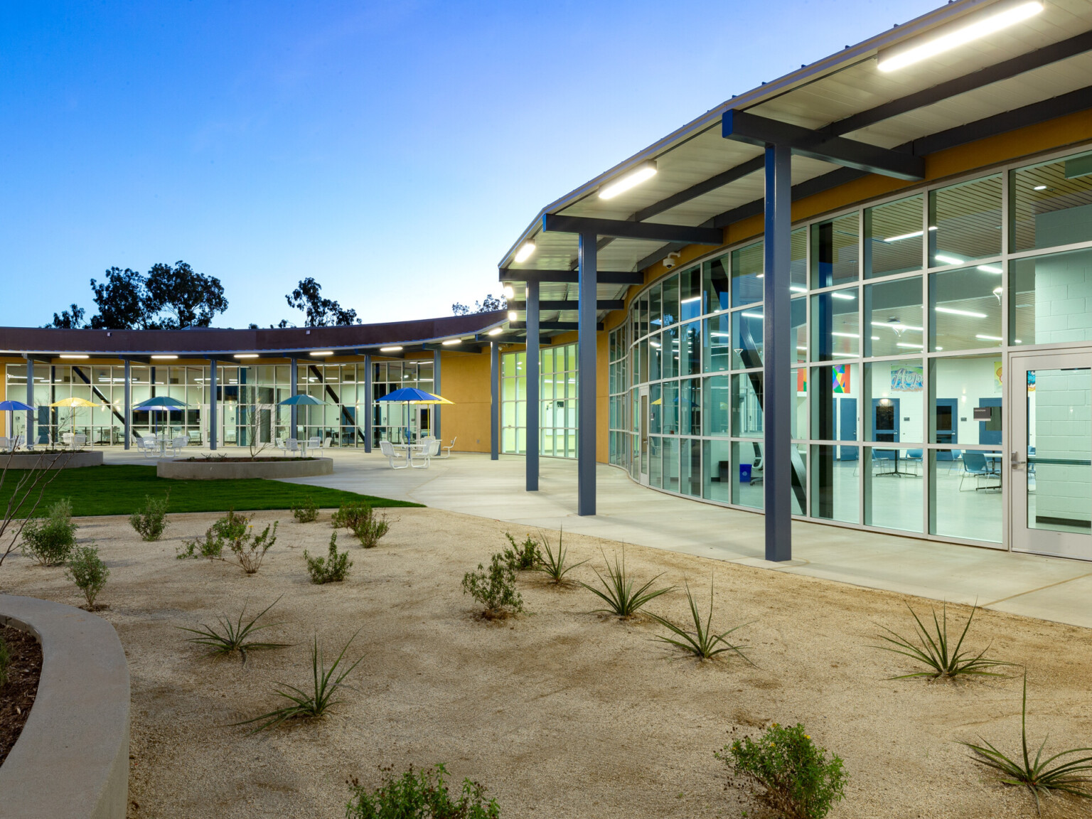 curved single story building with flat roof floor to ceiling glass facade with yellow panels. concrete paths in desertscape