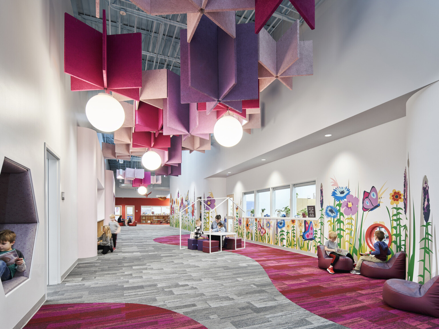 A brightly decorated children's hallway with hanging geometric light fixtures and colorful flower and butterfly wall art.