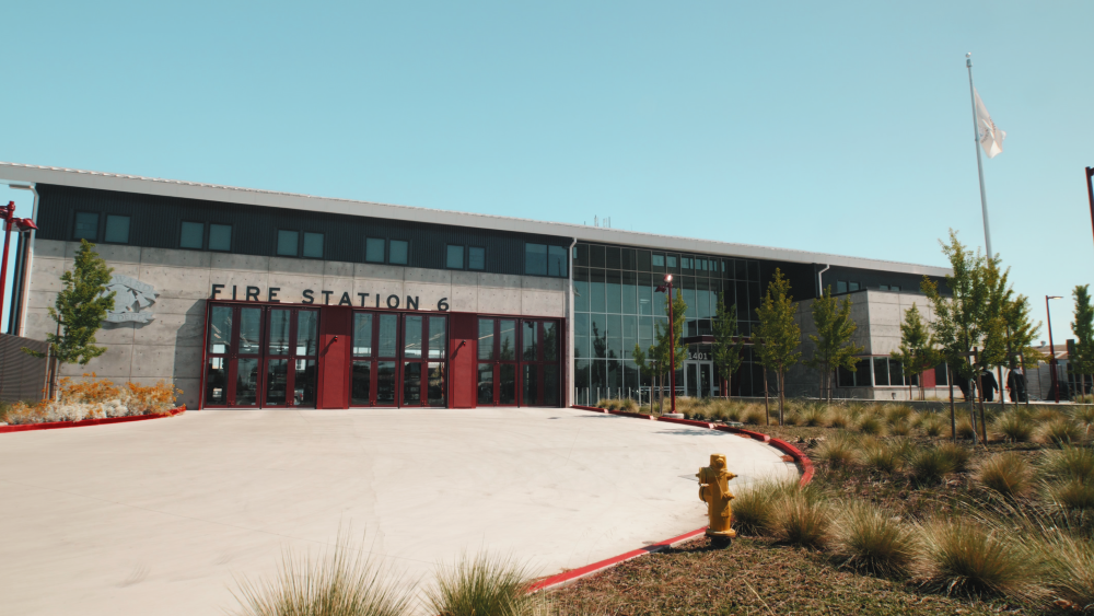 Exterior of white concrete a fire station with red accents. Words fire station 6 prominently displayed above the large glass doors.